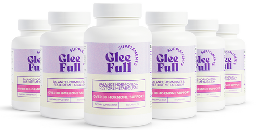 A product bundle display for GleeFull Supplements on a marble surface against a pink background. The layout includes a large purple shipping box featuring the slogan 'FEEL LIKE YOURSELF AGAIN.', three white bottles of Over 30 Hormone Support, a purple branded pen, a matching notepad that reads 'REMINDERS WHEN I'M HAVING A MENOPAUSE MOMENT', and a recipe booklet titled 'THE MENOPAUSE Recipes'