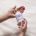A person holds a white GleeFull Meno Belly Flusher bottle in one hand while tan capsules rest in their open palm, set against a soft cream blanket background. The label reads 'Maintains Bloat Free Midsection, Meno Belly Flusher, 60 Capsules'.