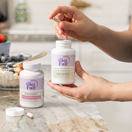 GleeFull Over 30 Hormone Support and Meno Joint Relief bottles on a marble countertop in a kitchen setting.
