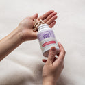 A person holds a white GleeFull Meno-Shred Fat Burner bottle in one hand while tan capsules rest in their open palm, set against a soft cream blanket background. The label reads 'Support Metabolism & Energy, Meno-Shred Fat Burner, 60 Capsules'.