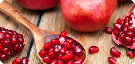 Pomegranate seeds in a wooden spoon on a wooden surface with whole pomegranates.